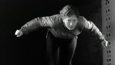 One of the skiers bends over in a skiing pose, with her arms out behind her, in the wind tunnel.