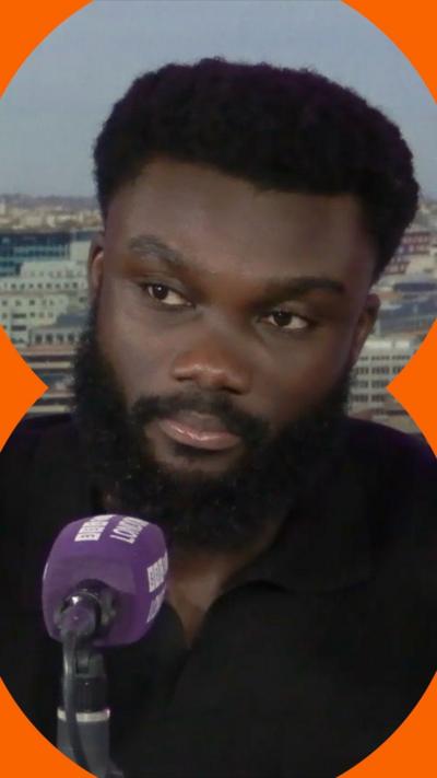 A person seated at a microphone, discussing against a backdrop of a city skyline.