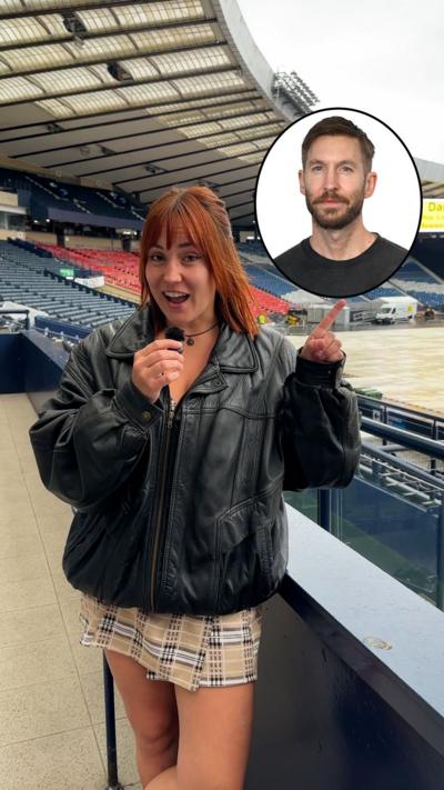 A young woman stands inside Hampden Park stadium in Glasgow, smiling and holding a small microphone. She has hazel eyes and shoulder-length auburn hair. She wears a black choker necklace and a black leather jacket over a beige tartan dress. Behind her are rows of red and blue seats and a partially covered pitch, with some vehicles visible on the ground. She’s pointing upward toward a circular inset showing a photo of Scottish DJ and producer Calvin Harris.