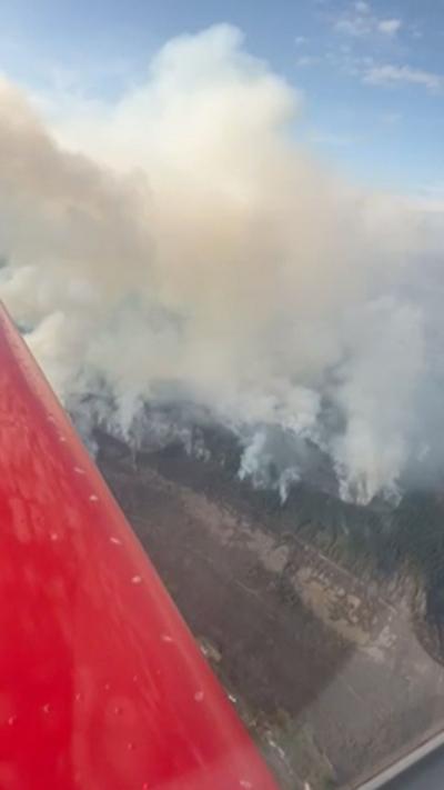 A huge plume of smoke and part of the red body of an aeroplane above a bare hill
