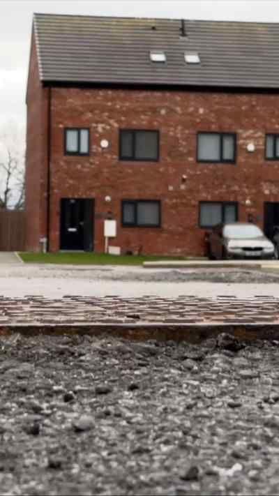 A new build home shot from a distance. In the foreground is an unpaved road.
