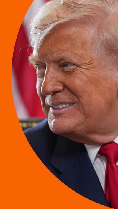Donald Trump smiles, looking to his right, in front of a US flag