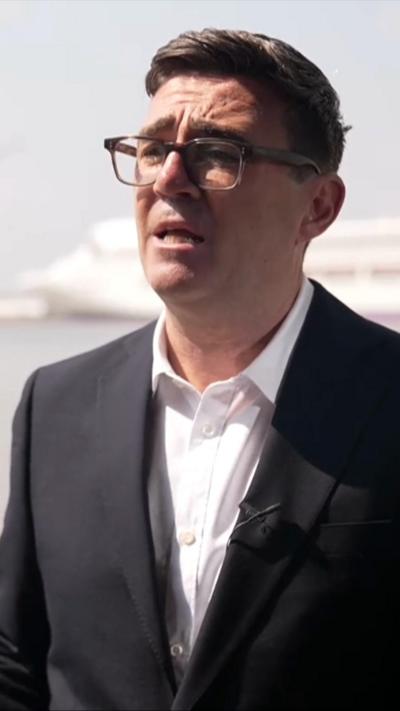 Burnham, in a white shirt and black suit jacket, speaks in front of the Kentish coastline