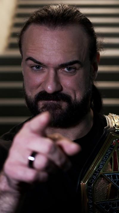 Drew McIntyre pointing at the camera and wearing the WWE title on his shoulder