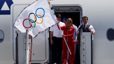 The Mayor of Los Angeles is holding the Olympic flag with a group of men standing behind her.