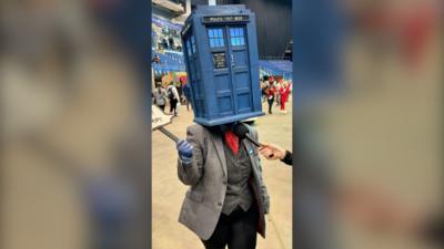 A person wearing a grey suit and a Doctor Who Tardis model over their head