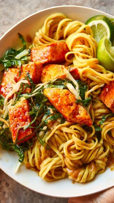 Top down view of tofu on a bed of noodles and veg in a white bowl