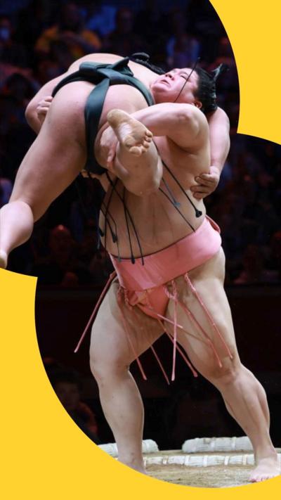 Midorifuji (L) is lifted by Ura (R) as they grapple during the Grand Sumo Tournament
