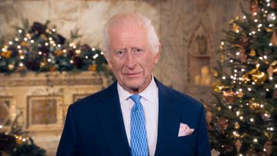 King Charles standing in the chapel decorated with Christmas trees and white lights.