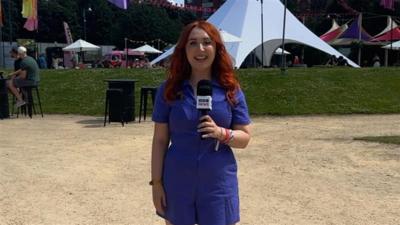 A woman in a blue dress with red hair standing in a sunny festival arena