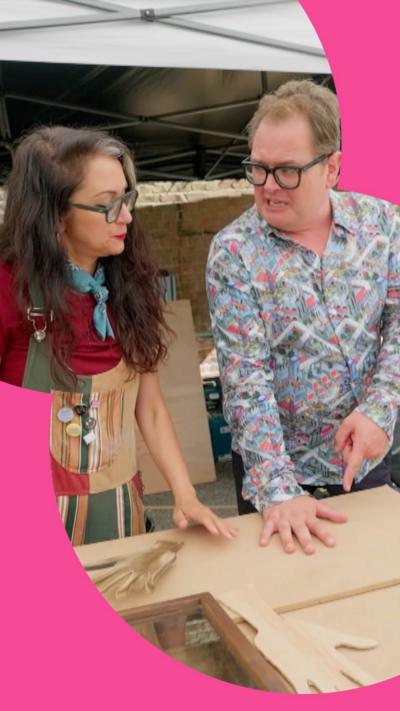 Alan Carr stands next to artist with his hand on a table ready to be drawn around 
