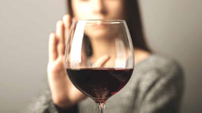 A glass of red wine in front of a person with their hand up