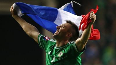 Gareth McAuley celebrates Northern Ireland's Euro 2016 qualification with the flag of finals hosts France