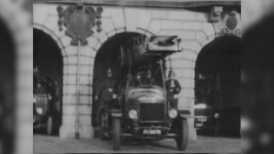 An old black and white picture shows firefighters on a fire engine as it leaves the fire station through a brick archway