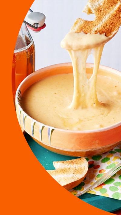 A bowl of melted cheese dip, with someone putting a bagel in it
