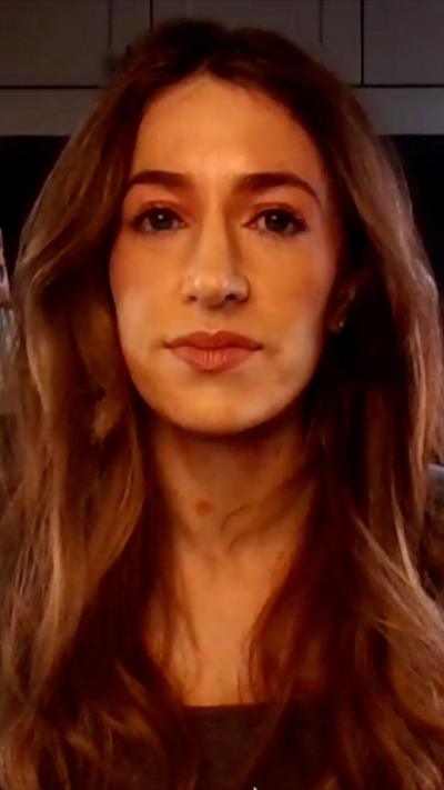 A woman with long wavy brown hair looks into the camera