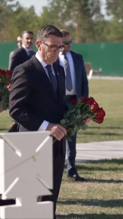 Burnham in a black suit holding flowers by a grave