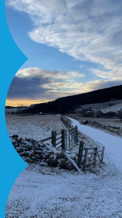 Country road with a covering of snow. Fields either side also dusted with snow.