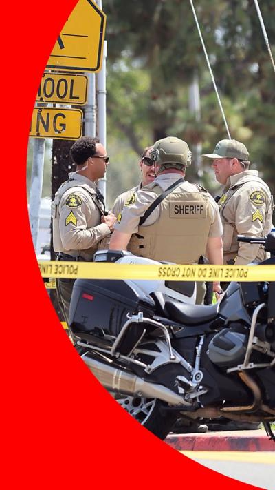 Four police officers stand behind tape