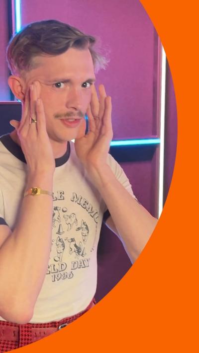 A man wearing a white t-shirt and red trousers stands with his hands against his face.