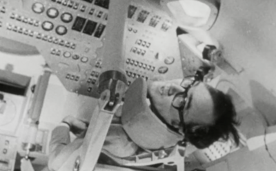 James Burke sits inside an Apollo space capsule simulator