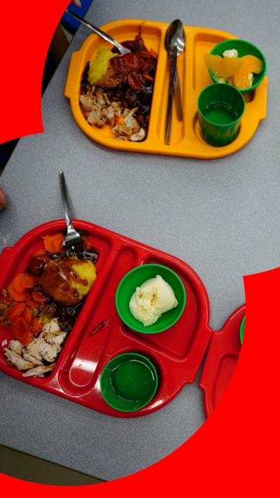 Two yellow and two red trays of school meals on a grey table, seen from above.