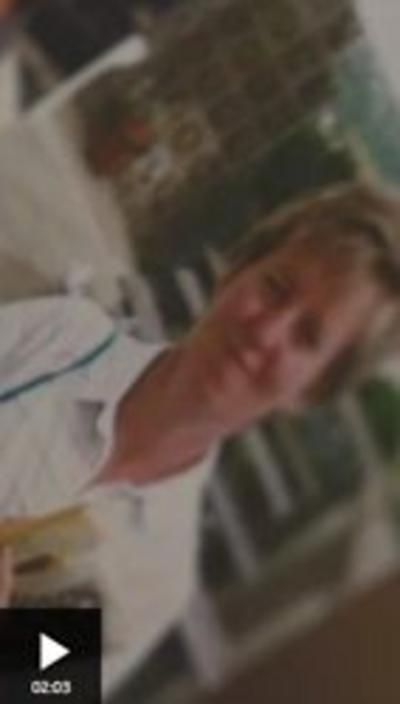 Blurred and old photo of a woman wearing a white shirt and holding a newspaper. She has dark blonde hair.