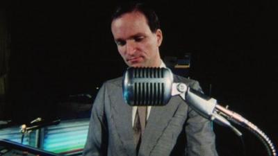 A member of the band Kraftwerk stands at a keyboard, behind a microphone