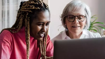 A girl wearing a red top looking at a laptop next to a elderly woman in a white top and glasses 