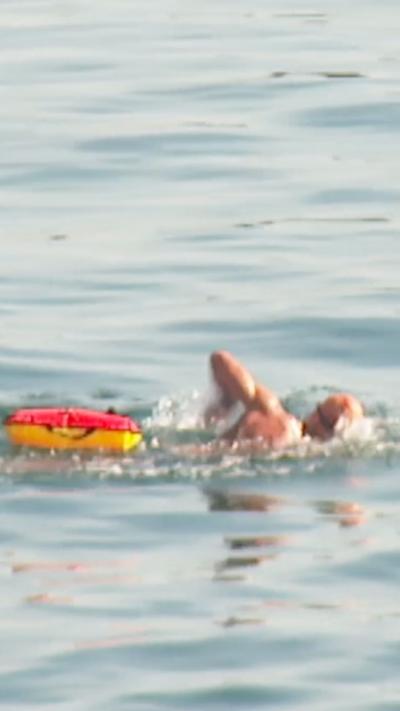 Man swimming in the sea with a red and yellow float beside him