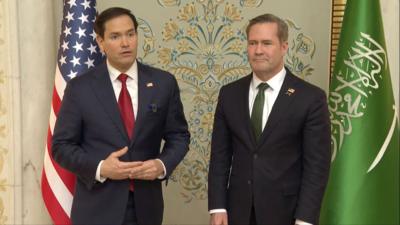 Marco Rubio and Mike Waltz standing in front of a US and Saudi flags