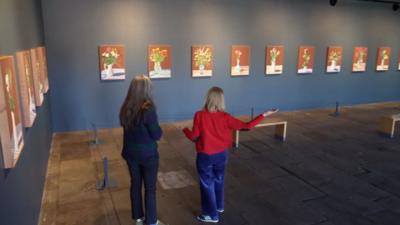 Person looking at a row a flower portrait on a grey wall in an art gallery