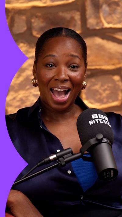 A woman with dark hair pulled back from her face talks into a microphone