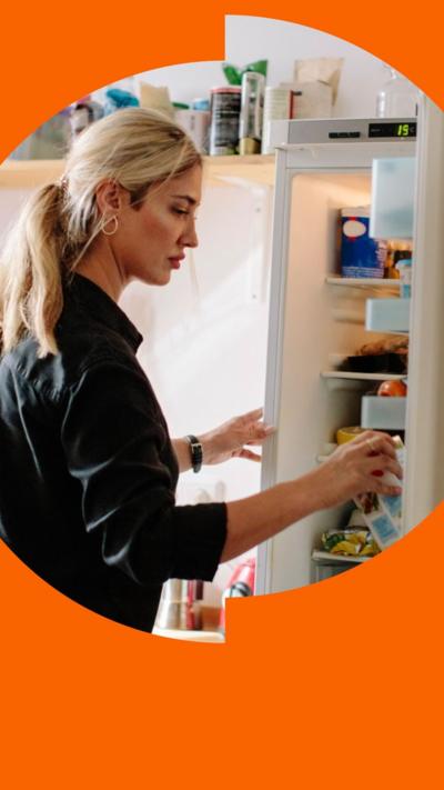 A woman grabs a carton of milk from an open fridge