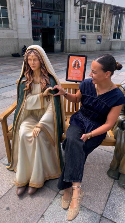 Reporter Tink Llewellyn making a heart sign with a statue of St Dwynwen