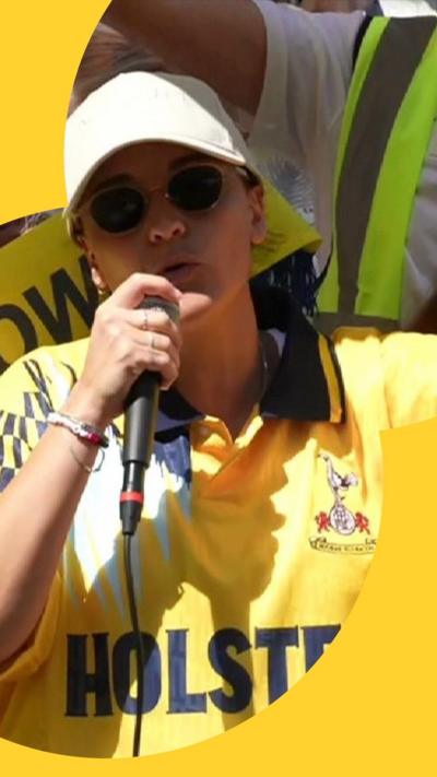 Emily Damari in a Spurs shirt and dressed in a baseball cap speaks through a microphone