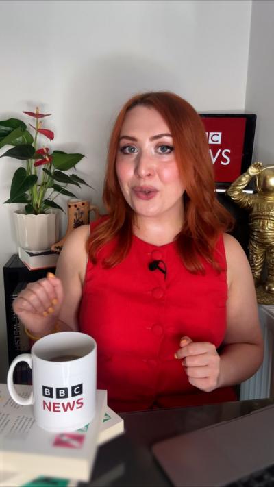 BBC's Alice Cruikshank who has long red hair and is wearing sleeveless red top and sitting at a table