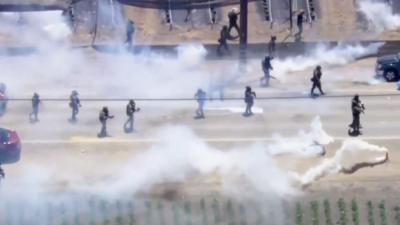 Aerial view of immigration agents deploying tear gas on protesters on a road.