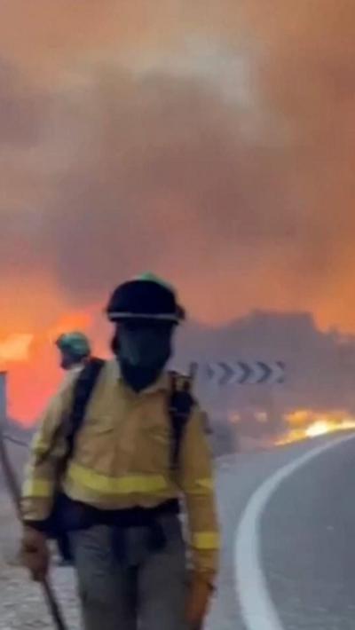 A firefighter beside a road with a wildfire behind