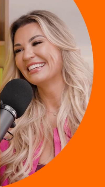 Christine McGuinness is smiling and wearing a pink jacket. She is sat in front of a mic and has her head tilted to the side.
