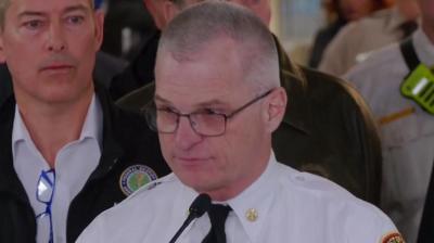 John Donnelly wearing smart uniform speaking into microphone with crowd standing behind him