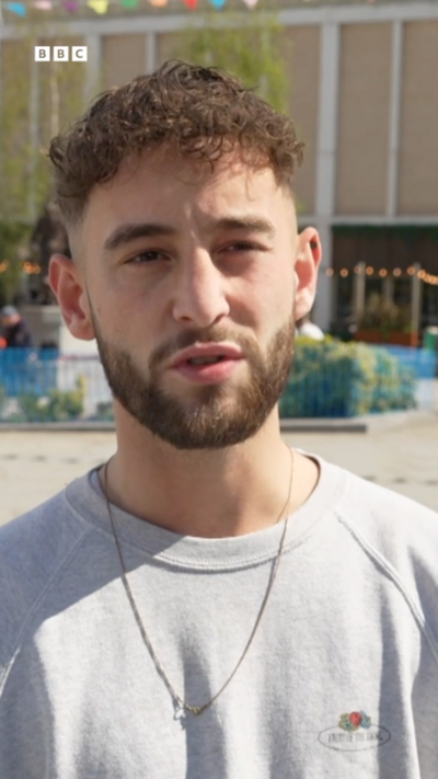 A man with short curly hair and a trimmed beard wears a grey sweatshirt and looks at the camera
