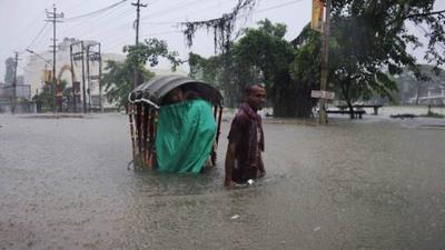 An Indian rickshaw puller transports a woman through a flooded street during a heavy downpour