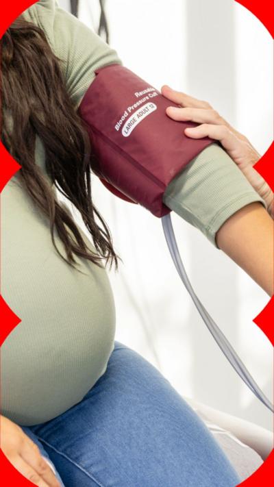 A pregnant woman wearing a long-sleeved green top has her blood pressure taken. 