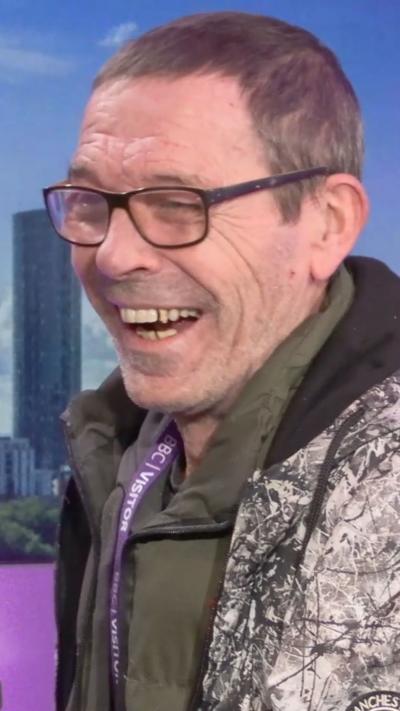 Mani's brother, Greg, smiling. He wears glasses, has short brown hair and is in a hoodie.