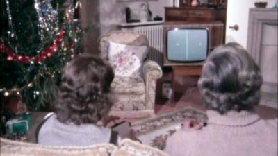 Two people play a ping-pong game on a games console in a living room decorated with a Christmas tree.