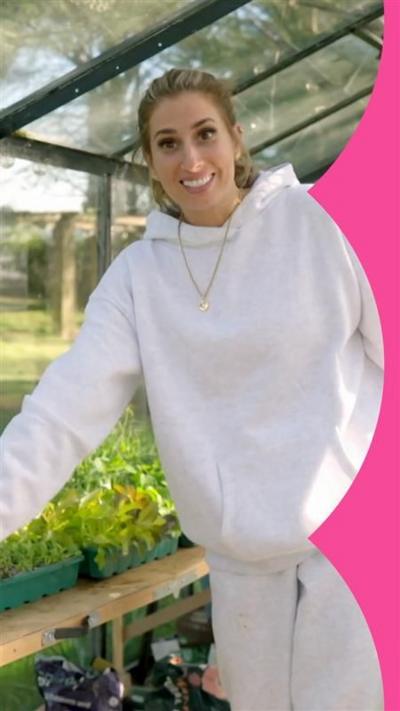 Stacey Solomon stands in a greenhouse, looking excited while pointing at vegetables. She wears a white tracksuit
