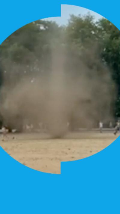 Swirling cloud of dust in a dry field with trees in the background.