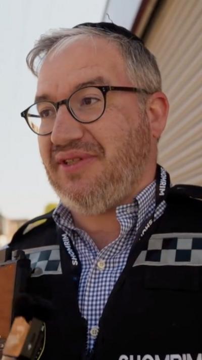 Isaac wearing glasses and a Shomrim vest over a shirt