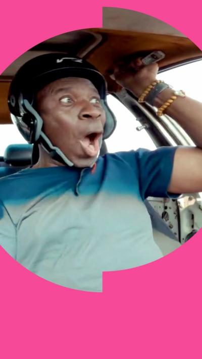 Clive Myrie looks elated in a car wearing a helmet and holding on to a handle